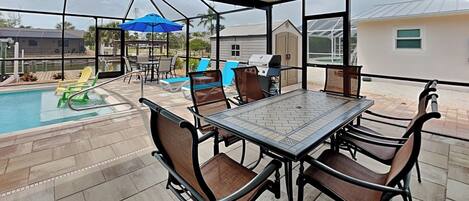 Eine überdachte Terrasse mit Pool, Gartenmöbeln und Grill.