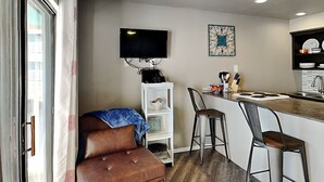 A compact kitchen with a bar area, a television mounted on the wall, and a small seating area with a sofa and bar stools. - Villa Del Sol #2138 by Miss Kitty’s (Corpus Christi)