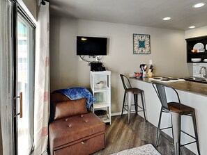 A compact kitchen with a bar area, a television mounted on the wall, and a small seating area with a sofa and bar stools. - Villa Del Sol #2138 by Miss Kitty’s (Corpus Christi)