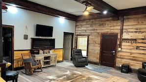 Una sala de estar con techo de madera, televisor de pantalla plana, sillón de cuero, mesa de centro de madera y alfombra de cuero.