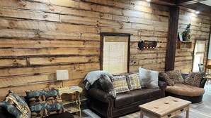Una sala de estar acogedora con una pared de troncos de madera, un sofá de cuero marrón, una mesa de centro de madera y un otomano estampado.