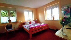 Un dormitorio con una cama, una silla, un escritorio y dos ventanas.