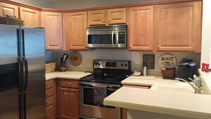 A kitchen with wooden cabinets, a stainless steel refrigerator, a microwave, an oven, and a coffee maker. - Prime Location! Ski In, Ski Out 3BDR plus bonus room, 3BA, Condo on Dobie (Wintergreen Resort)