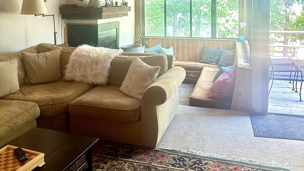 A living room with a sofa, coffee table, and a fireplace. There is a large window with a view of greenery outside. - Prime Location! Ski In, Ski Out 3BDR plus bonus room, 3BA, Condo on Dobie (Wintergreen Resort)