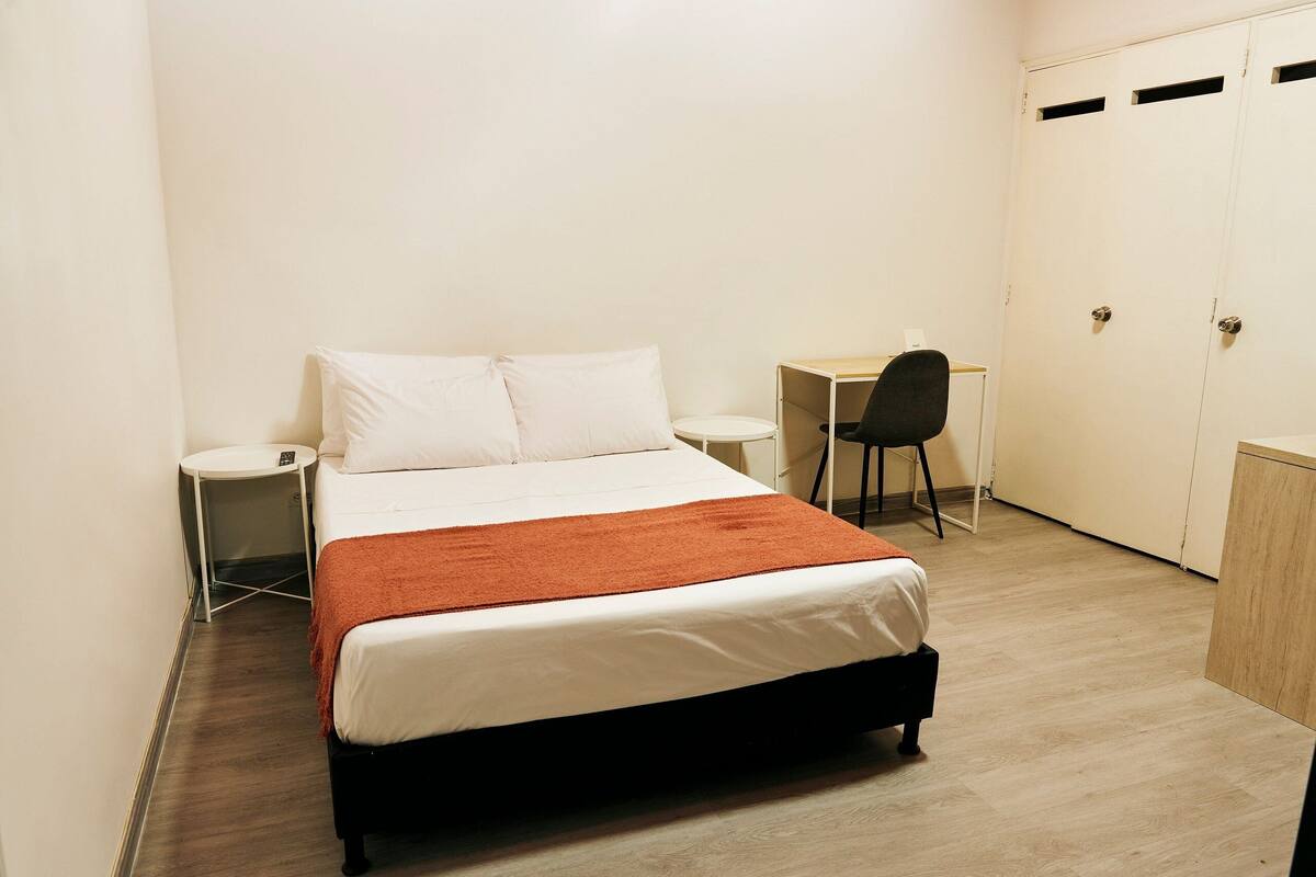 A neatly arranged bedroom with a bed, a desk, and a chair.