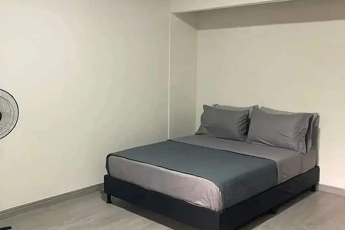 A bedroom with a bed, a standing fan, and a sloped ceiling.