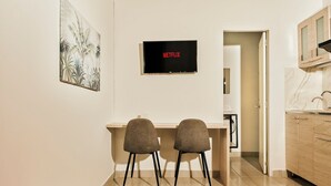 Una cocina moderna con un televisor integrado que muestra 'NETFLIX', dos sillas junto a una pequeña mesa de comedor y un armario de cocina con encimera de mármol.