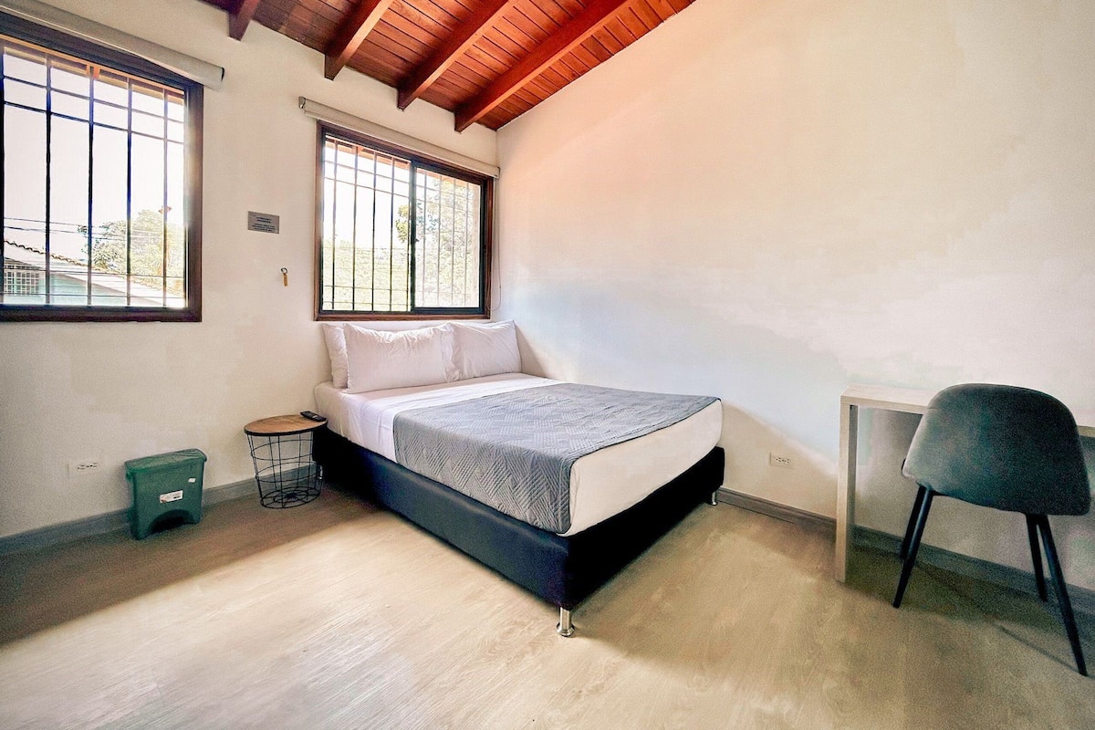 A bedroom with a bed, two windows, a chair, and a radiator.