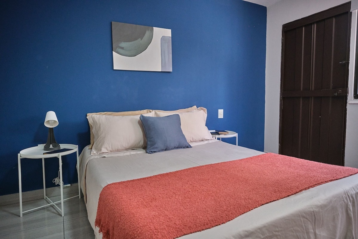 A bedroom with a bed, a nightstand, a lamp, a painting on the wall, and a door.