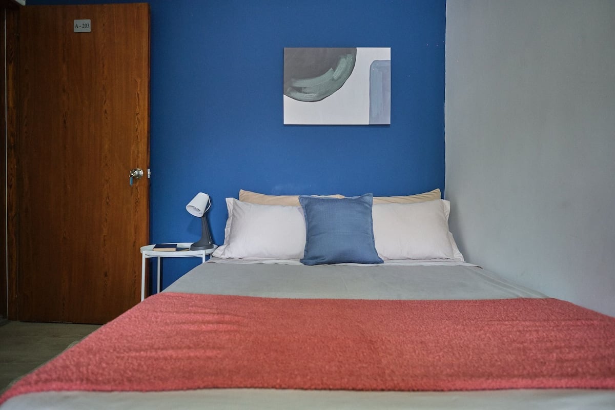 A bedroom with a bed, a nightstand, a lamp, and a painting on the wall.