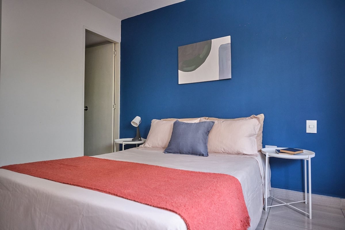 A bedroom with a bed, a nightstand, a lamp, and a painting on the wall.
