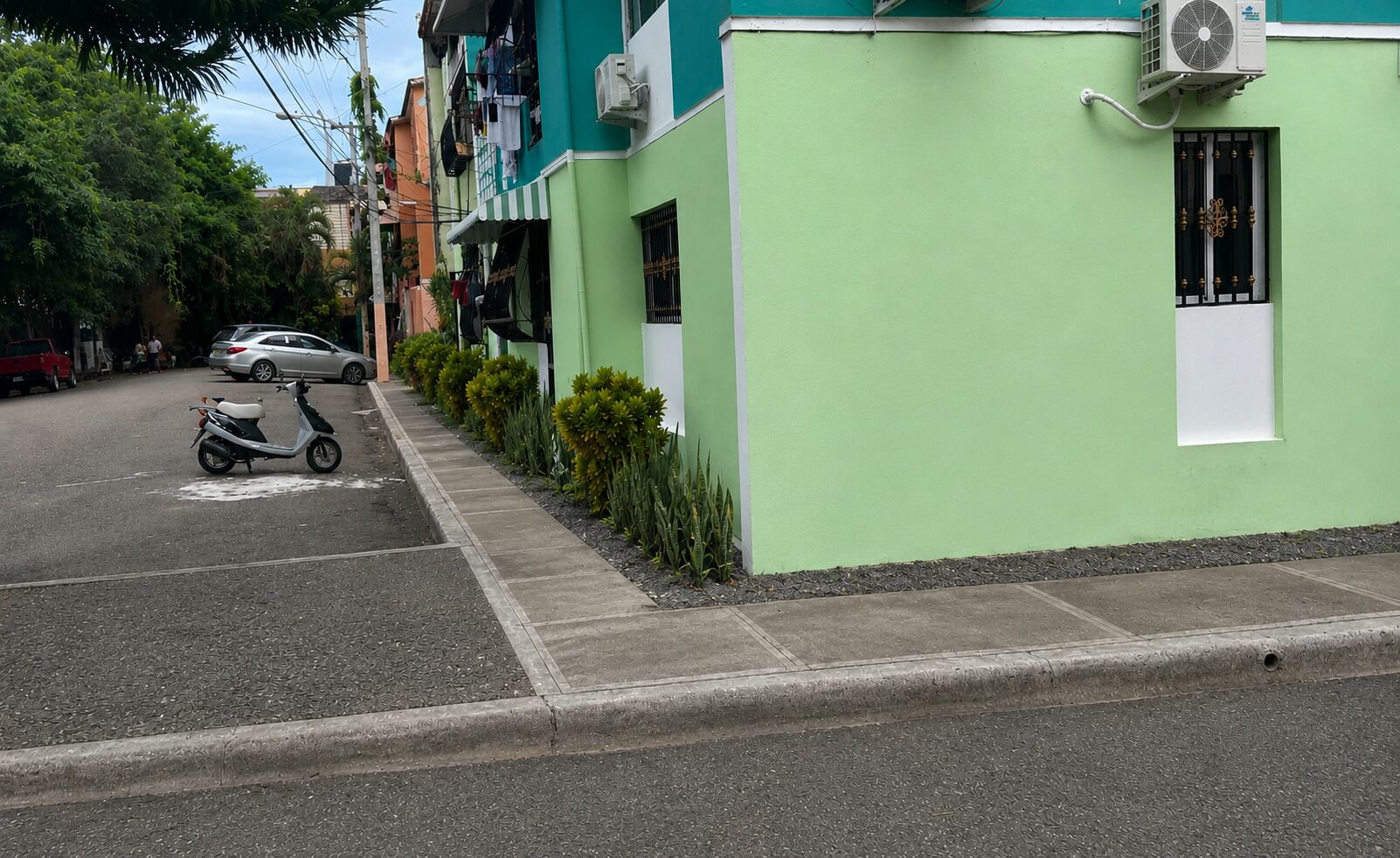 A street view with a green building, a parked scooter, and a car.