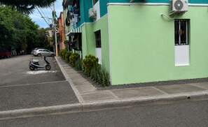 Vista de la calle con un edificio verde, una moto estacionada y un coche.