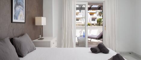 A hotel room with a bed, a nightstand, a lamp, and a view of the outside.
