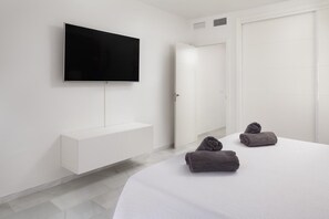 A hotel room with a bed, a TV mounted on the wall, a white wardrobe, and a door.