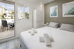 A hotel room with a bed, a chair, a table, and a view of the city through a large window.
