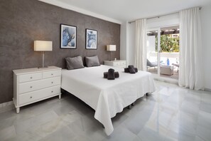 Quarto moderno com uma cama grande, duas mesas de cabeceira, uma cômoda e vista para área externa.