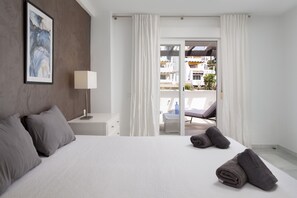 Quarto moderno com cama grande, mesa de cabeceira com abajur e vista para a varanda.