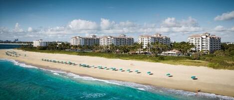 A beachfront hotel with multiple buildings, a sandy beach, and a clear blue ocean.