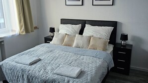Una cama bien hecha con cubrecama acolchado, dos mesitas de noche con lámparas y dos cuadros enmarcados en la pared.