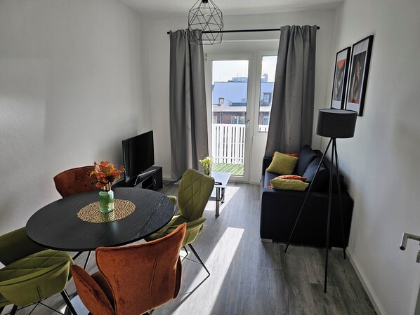 Ein modernes Wohnzimmer mit einem runden Esstisch, einer Couch und einem Fernseher.