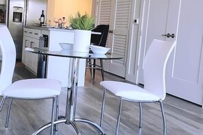 Cozinha moderna com armários brancos, uma mesa de vidro e duas cadeiras brancas.