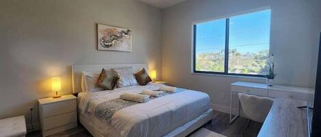 A bedroom with a bed, bedside tables, a desk, and a large window.