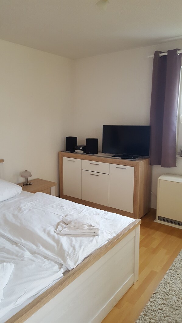 Une chambre d’hôtel avec un lit, une commode en bois, un téléviseur et un radiateur.