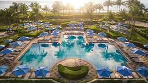 A pool area with lounge chairs and umbrellas, surrounded by palm trees and a view of the ocean. - Singer Island | Coastal Escape | Pools & Beach Days (Palm Beach Shores)