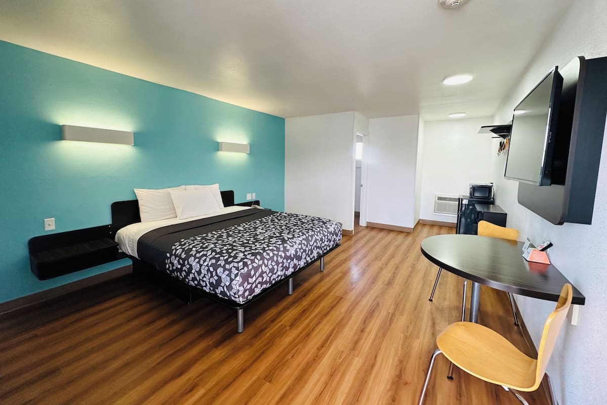 A hotel room with a bed, a desk, a chair, a TV, and a microwave.