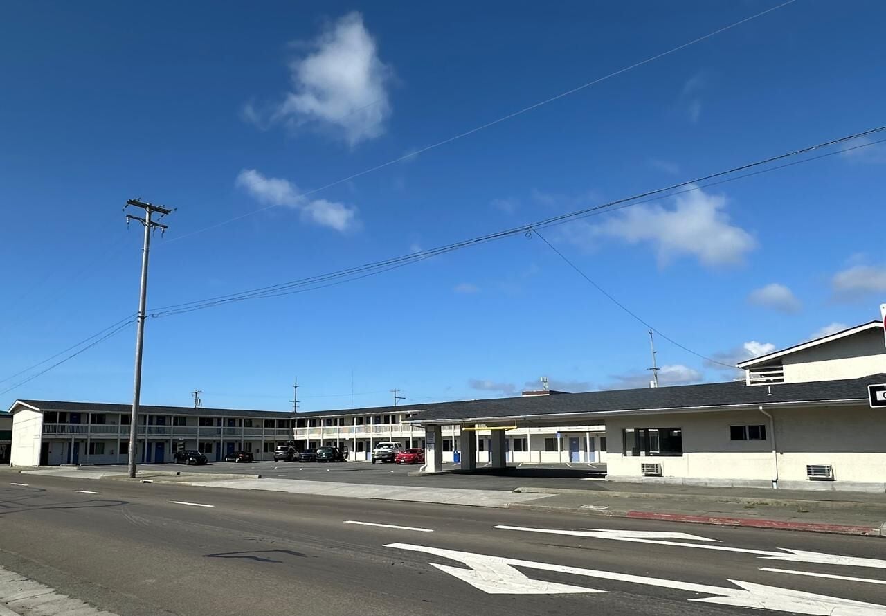 A motel with multiple rooms, a parking lot, and a clear blue sky.