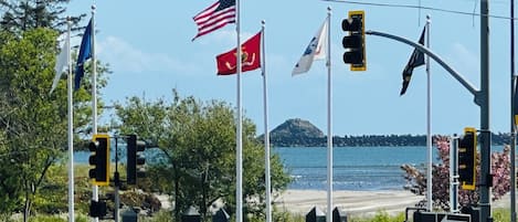 A coastal intersection with multiple traffic lights, a pedestrian crossing, and several flags including the American flag.