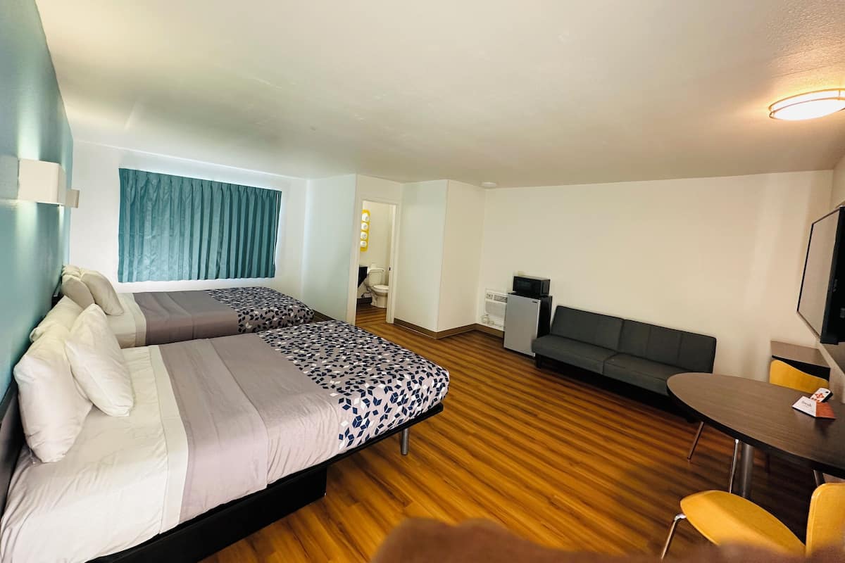 A hotel room with two beds, a sofa, a small table, and a TV.