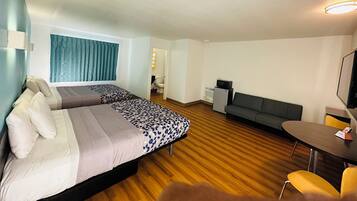 A hotel room with two beds, a sofa, a small table, and a TV.