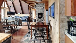 A cozy, rustic interior with a dining area, a stone fireplace, and a living room with a large sofa and television. - Special Memories by Taylor Made Deep Creek (Swanton)