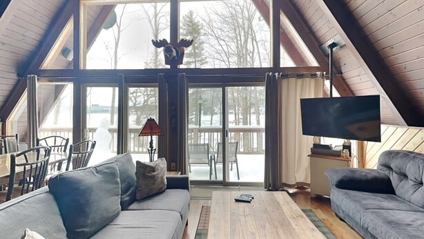A spacious loft with a high ceiling, a large sliding glass door leading to a deck, a sofa, a coffee table, and a TV. - Special Memories by Taylor Made Deep Creek (Swanton)