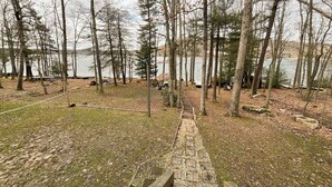 A wooden deck leading to a stone staircase surrounded by trees and a lake. - Special Memories by Taylor Made Deep Creek (Swanton)