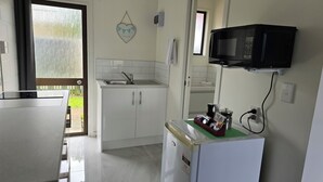 A compact kitchen with white cabinets, a stainless steel sink, a microwave, and a refrigerator. - Marton Motel NZ (Marton)