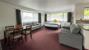 A hotel room with a bed, a sofa, a dining table with chairs, and a small desk. - Marton Motel NZ (Marton)
