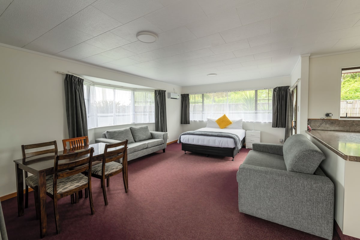 A hotel room with a bed, a sofa, a dining table with chairs, and a small desk.