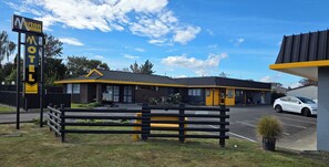 A motel with a signboard, a parking lot, and a building with a yellow roof. - Marton Motel NZ (Marton)