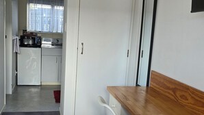 A compact kitchen with white cabinets, a microwave, and a refrigerator. There is a dining area with a wooden table and two white chairs. - Marton Motel NZ (Marton)