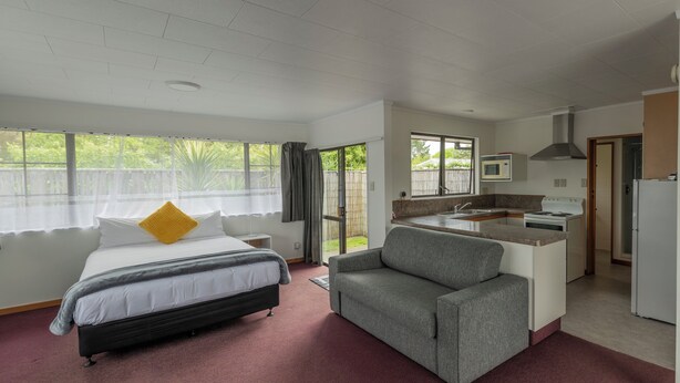 A bedroom with a bed, a grey armchair, a kitchenette with a stove and microwave, and a bathroom visible through an open door. - Marton Motel NZ (Marton)