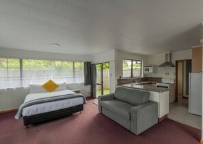 A bedroom with a bed, a grey armchair, a kitchenette with a stove and microwave, and a bathroom visible through an open door. - Marton Motel NZ (Marton)