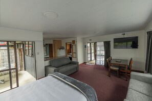 A hotel room with a bed, a sofa, a dining table with chairs, a TV, and a sliding glass door leading to a balcony. - Marton Motel NZ (Marton)