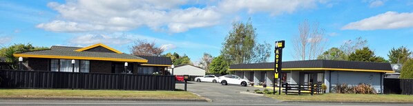 A motel with a yellow and black facade, a fenced parking area, and a clear blue sky. - Marton Motel NZ (Marton)