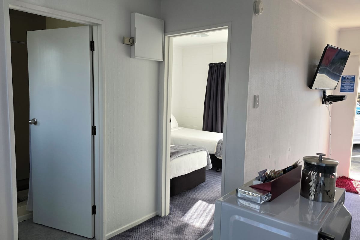 A hotel room with a bed, a desk with a computer, a mirror, and a door leading to another room.