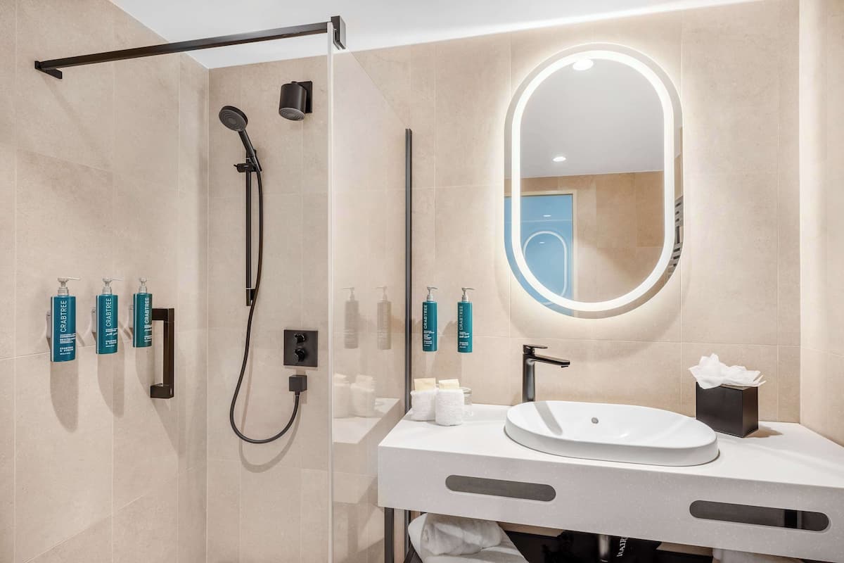 Un baño moderno con ducha de vidrio, lavabo blanco y un espejo grande.