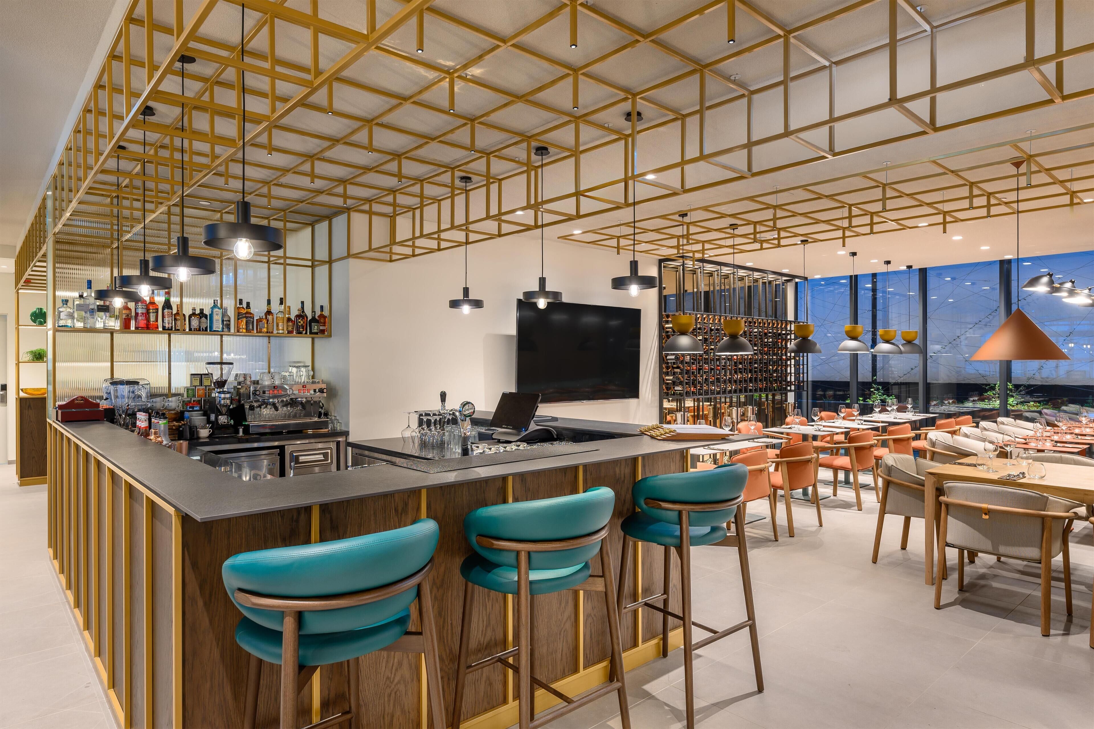 A modern bar area with a long counter, bar stools, and a large TV screen.