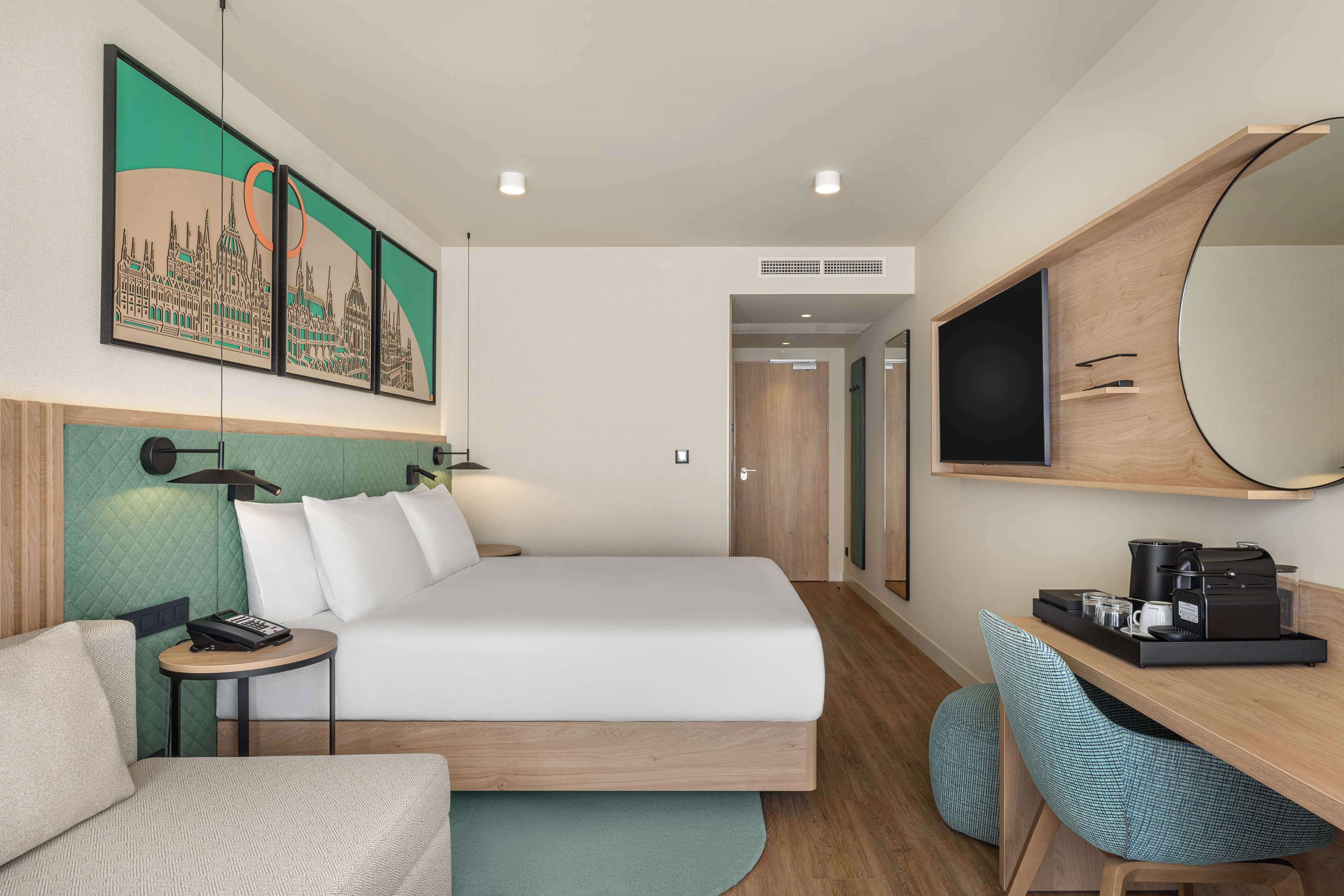 Une chambre d’hôtel comprenant un lit, un bureau avec une machine à café, une chaise, une petite table et un grand miroir.